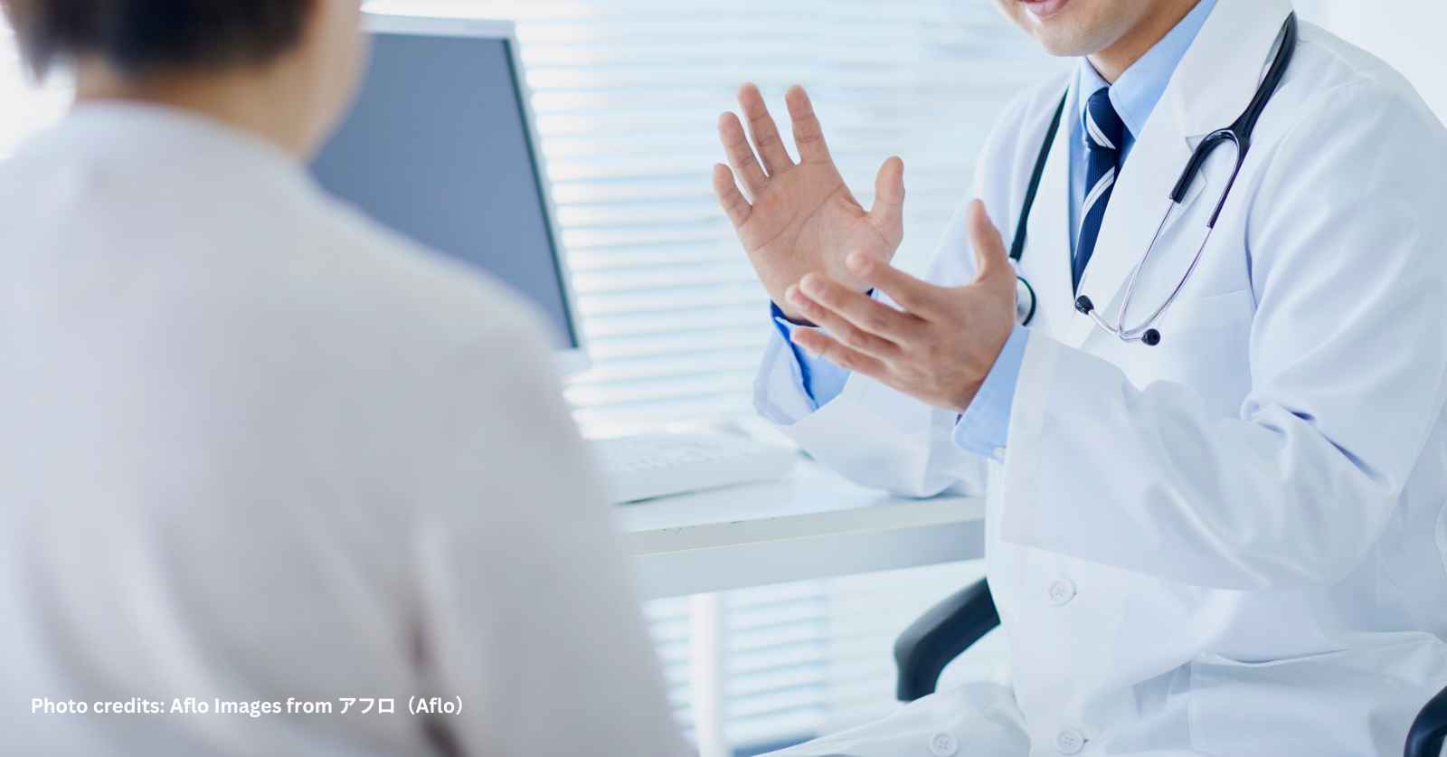 A hospital pharmacist, doctor, or nurse sitting with a patient (possibly elderly), reviewing medications or a discharge summary together.