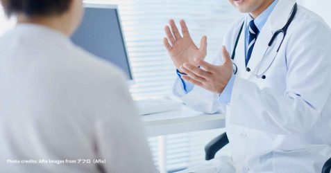 A hospital pharmacist, doctor, or nurse sitting with a patient (possibly elderly), reviewing medications or a discharge summary together.